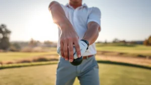 Professional golfer demonstrating proper grip and stance setup on a practice range with morning sunlight, showing hand positioning and body alignment clearly from address position perspective
