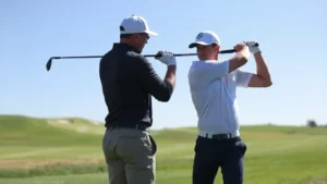 Professional golfer receiving swing instruction from certified coach on practice range with clear blue sky and manicured fairway in background, demonstrating proper grip and posture