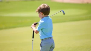 Young child in proper golf stance on sunny course with green fairway, holding junior golf club, focused expression, professional instruction setting