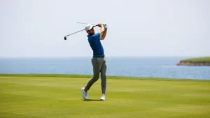 Professional golfer mid-swing on manicured fairway with water hazard visible in background, lush green grass, natural lighting, focused expression